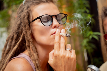 Young hippie woman in sunglasses smoking a joint