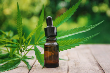 Cannabis tincture on a wooden table with a cannabis leaf behind it