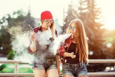 Two girls smoking outside chilling by the fence